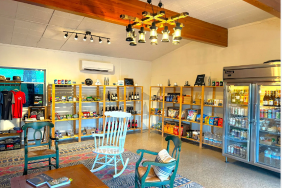 Cozy store interior with wooden shelves, chairs, and a fridge filled with beverages.