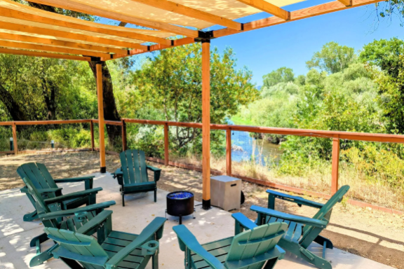 Outdoor patio with chairs, table, and pergola overlooking a river and trees.